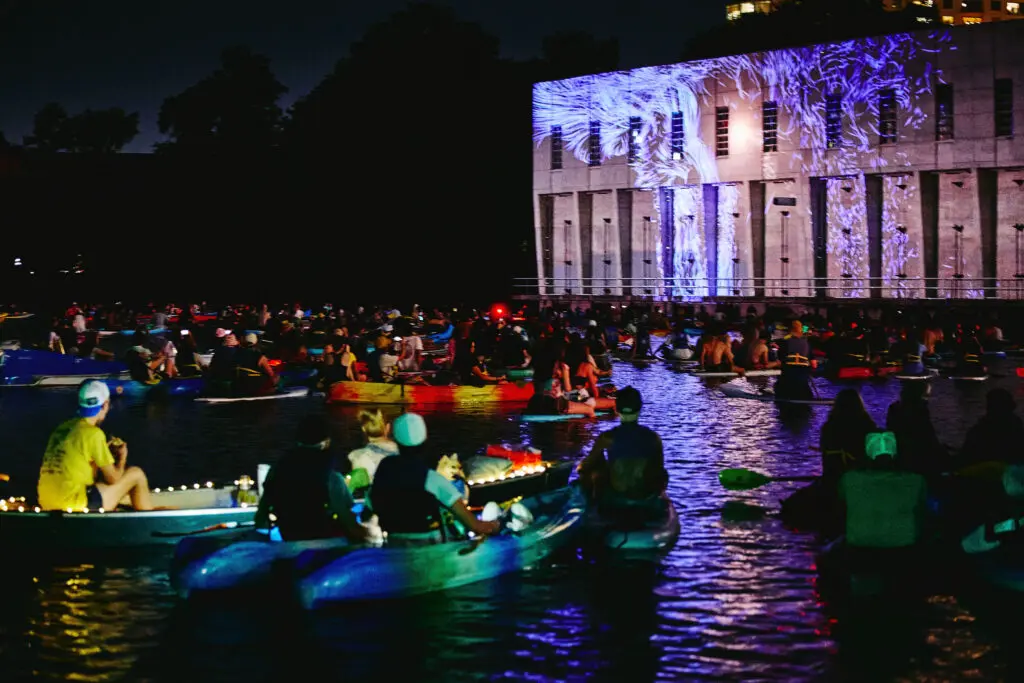 Kayakers on Lady Bird Lake watching WaterWork projections on the Seaholm Intake Facility